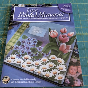 May include: A book titled "Jan's Painted Memories" with floral illustrations of daisies, tulips, and violets. The cover also features the text "See how we grow" and "20 painted projects to beautify album covers, frames, scrapbook pages, etc."