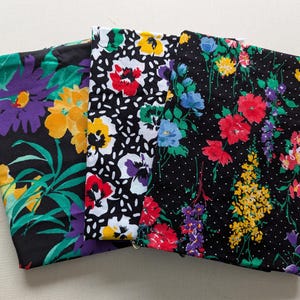 May include: Four fabric swatches with floral patterns on a black background. The patterns include purple, yellow, red, blue, and green flowers.