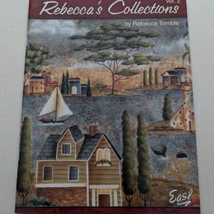 Può includere: Copertina del libro "Rebecca's Collections Vol. 2" di Rebecca Trimble. L'illustrazione raffigura un paesaggio con case, alberi, una barca a vela e un faro. La tavolozza dei colori comprende sfumature di marrone, blu e verde.