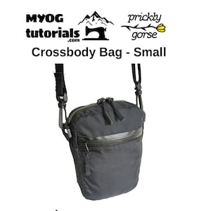 Könnte beinhalten: Schwarze Umhängetasche in kleiner, rechteckiger Form. Sie hat ein Hauptfach mit Reißverschluss und eine Vordertasche mit Reißverschluss. Inklusive verstellbarem Riemen. Der Text "Crossbody Bag - Small" ist sichtbar.