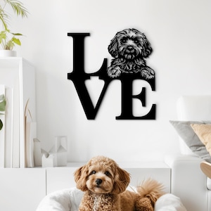 May include: A black metal wall art piece spelling "LOVE" with a dog silhouette in the "O". A brown dog rests in a white dog bed on a wooden floor. The room has white walls and a white sofa.