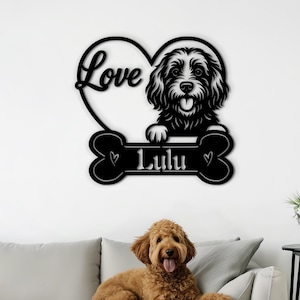 May include: Black metal wall art featuring a dog's face emerging from a heart shape with the word "Love" and a bone shape with the name "Lulu". A golden doodle dog is lying on a gray sofa in front of the wall art.