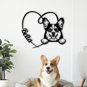 May include: A black metal wall art piece featuring a Corgi dog inside a heart shape with the name "Bella". A live Corgi dog sits in a gray dog bed. The dog has brown and white fur.