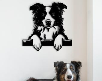 May include: Black and white border collie dog peeking over a wall, with a similar dog lying on a beige dog bed in the foreground.