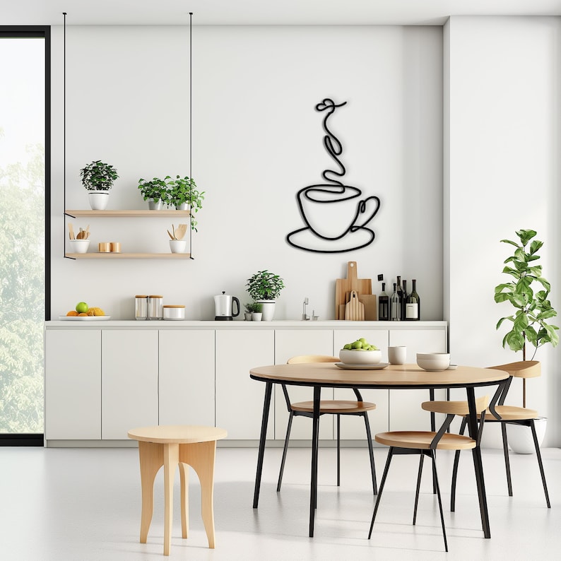May include: Black metal wall art depicting a stylised coffee cup with steam rising from it. The art is hanging on a white wall in a kitchen setting.