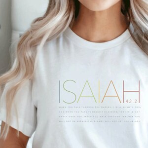 May include: White t-shirt with the text "ISAIAH 43:2" and a Bible verse printed in colorful text. The verse reads "When you pass through the waters, I will be with you; and when you pass through the rivers, they will not sweep over you. When you walk through the fire, you will not be burned; the flames will not set you ablaze."