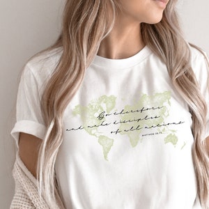 Op de afbeelding: Wit T-shirt met een groene wereldkaart afbeelding en de tekst "Ga daarom en maak discipelen van alle volken" met de bijbelverwijzing "Matthe&uuml;s 28:19".