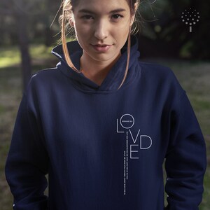 May include: Navy blue hoodie with a white graphic that says "Loved" with the Bible verse "Romans 5:8 But God demonstrates His own love for us in this: While we were still sinners, Christ died for us."
