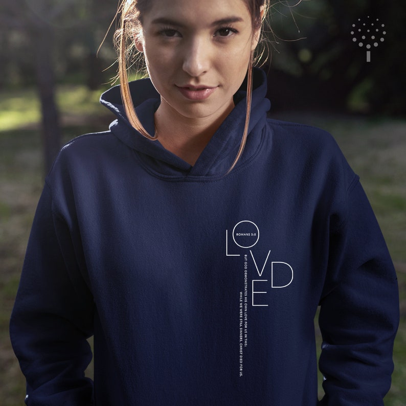 May include: Navy blue hoodie with a white graphic that says "Loved" with the Bible verse "Romans 5:8 But God demonstrates His own love for us in this: While we were still sinners, Christ died for us."