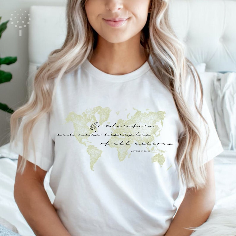Op de afbeelding: Wit T-shirt met een gouden omtrek van een wereldkaart en de tekst "Ga daarom heen en maak alle volken tot mijn discipelen. Matthe&uuml;s 28:19"