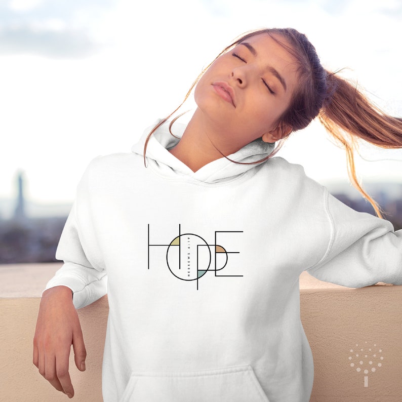 May include: White hoodie featuring a graphic design of the word "HOPE" in black and white with a circle in the centre of the word. The circle is filled with various colours, including beige, light blue, and yellow.