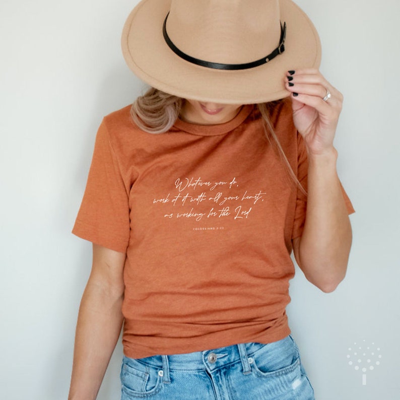 May include: A rust-colored t-shirt with a white graphic print of a bible verse: "Whatever you do, work at it with all your heart, as working for the Lord."  Colossians 3:23