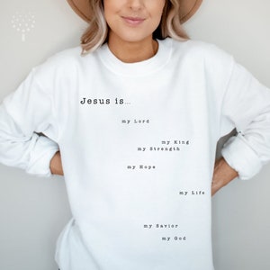 May include: White sweatshirt with the text "Jesus is..." followed by a list of phrases describing Jesus, including "my Lord", "my King", "my Strength", "my Hope", "my Life", "my Savior", and "my God".