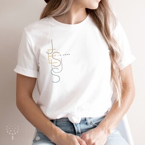 May include: White t-shirt with a graphic design of the word "JESUS" in a vertical, stylized font with the words "IS LORD" in smaller font above the "S".