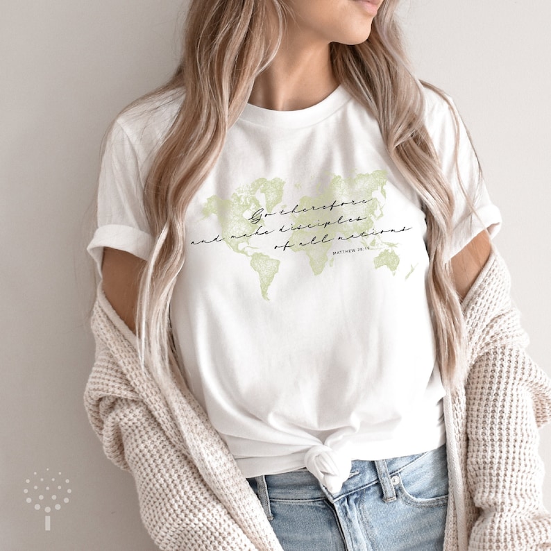 Op de afbeelding: Wit T-shirt met een groene wereldkaart afbeelding en de tekst "Ga daarom en maak discipelen van alle volken" met de bijbelverwijzing "Matthe&uuml;s 28:19".