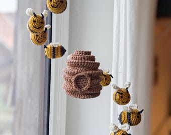 May include: A crocheted bee-themed baby mobile with a brown beehive and yellow and black bees hanging from a wooden ring.