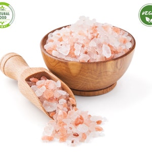 Pu&ograve; includere: Una ciotola di legno piena di sale rosa dell'Himalaya, con una paletta di legno e un piccolo mucchio di sale che si rovescia. La ciotola e la paletta sono su uno sfondo bianco. Le etichette "100% NATURAL FOOD" e "VEGAN" sono visibili nell'immagine.