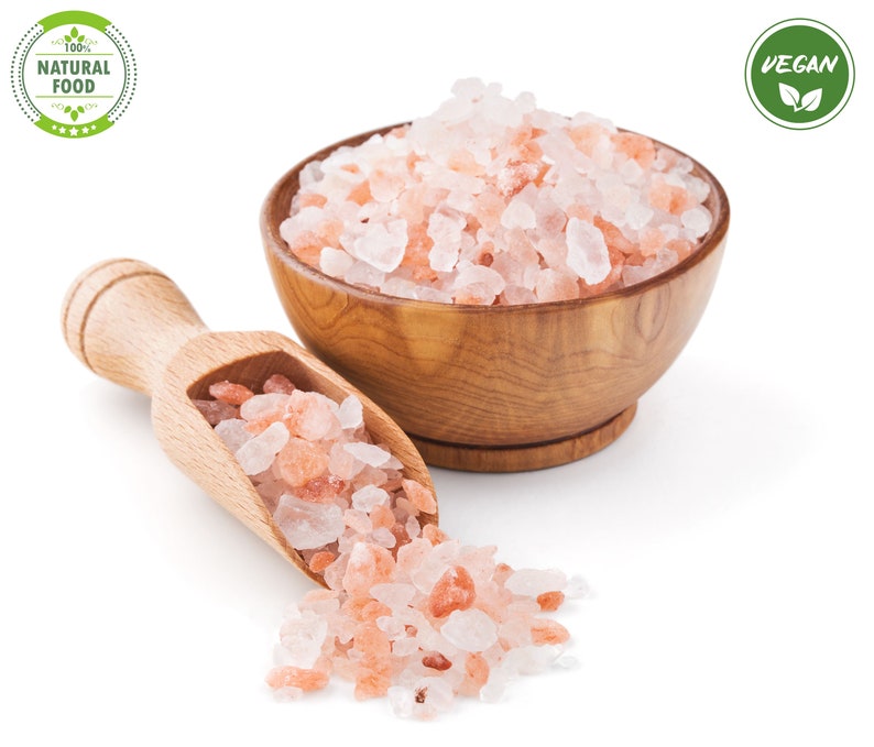 Pu&ograve; includere: Una ciotola di legno piena di sale rosa dell'Himalaya, con una paletta di legno e un piccolo mucchio di sale che si rovescia. La ciotola e la paletta sono su uno sfondo bianco. Le etichette "100% NATURAL FOOD" e "VEGAN" sono visibili nell'immagine.