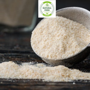 May include: A close-up of a white powder, likely tapioca starch, being poured from a metal measuring spoon onto a dark wooden surface. The powder is labeled as vegan, 100% natural food, and USDA organic.