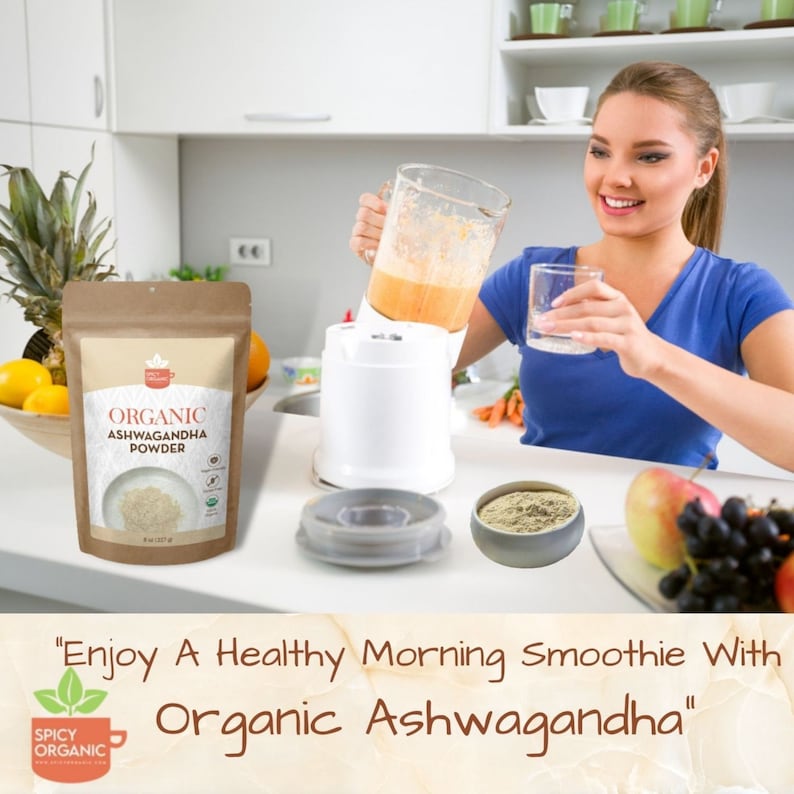 May include: A brown paper bag with a white label that reads "ORGANIC ASHWAGANDHA POWDER". The bag is sitting on a white worktop next to a blender with a glass jug filled with a light orange smoothie. A woman is holding a glass of the smoothie and smiling. The text "Enjoy A Healthy Morning Smoothie With Organic Ashwagandha" is written in brown text on a light brown background.