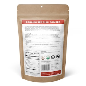 Op de afbeelding: Een bruine papieren zak met een label waarop "Organic Red Chili Powder" staat. Het label bevat een voedingssamenstelling, ingredi&euml;nten, instructies en bewaarinformatie. De zak heeft ook USDA Organic en SBE certificeringen.