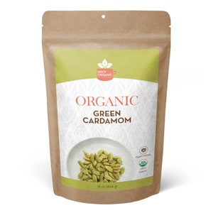 May include: A brown paper bag of organic green cardamom. The bag has a green and white label with the words "Organic Green Cardamom" and "Spicy Organic". The bag contains 16 oz (454 g) of cardamom and is labeled as vegan friendly and USDA organic.