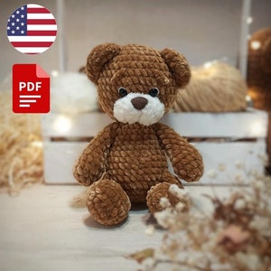 May include: A brown crocheted teddy bear sitting on a wooden surface. The bear has a white face and brown eyes. The image includes the text "PDF PATTERN" and a US flag.