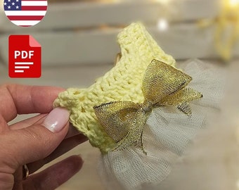 May include: A crochet baby dress pattern in PDF format. The dress is yellow with a gold bow and a white tulle skirt. The pattern is available for download.