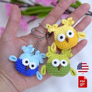 Pode incluir: Três chaveiros de coruja de crochê feitos à mão em azul, amarelo e verde. Cada coruja tem olhos brancos grandes, um bico marrom e pequenas asas. Os chaveiros são presos a argolas de metal prateado. As corujas têm aproximadamente 5 cm de altura.