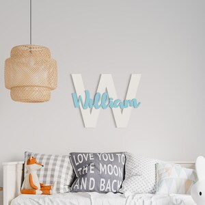K&ouml;nnte beinhalten: Wei&szlig;er Holzbuchstabe W mit dem Namen "William" in hellblauer Farbe. Der Buchstabe h&auml;ngt an einer wei&szlig;en Wand &uuml;ber einem wei&szlig;en Bett mit Kissen und einem Stofffuchs. Eine H&auml;ngeleuchte aus Weidengeflecht h&auml;ngt &uuml;ber dem Bett.