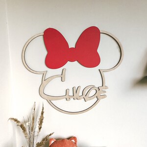 May include: Wooden wall decor featuring a silhouette of Mickey Mouse's head with a red bow and the name "Chloe" written in a cursive font.