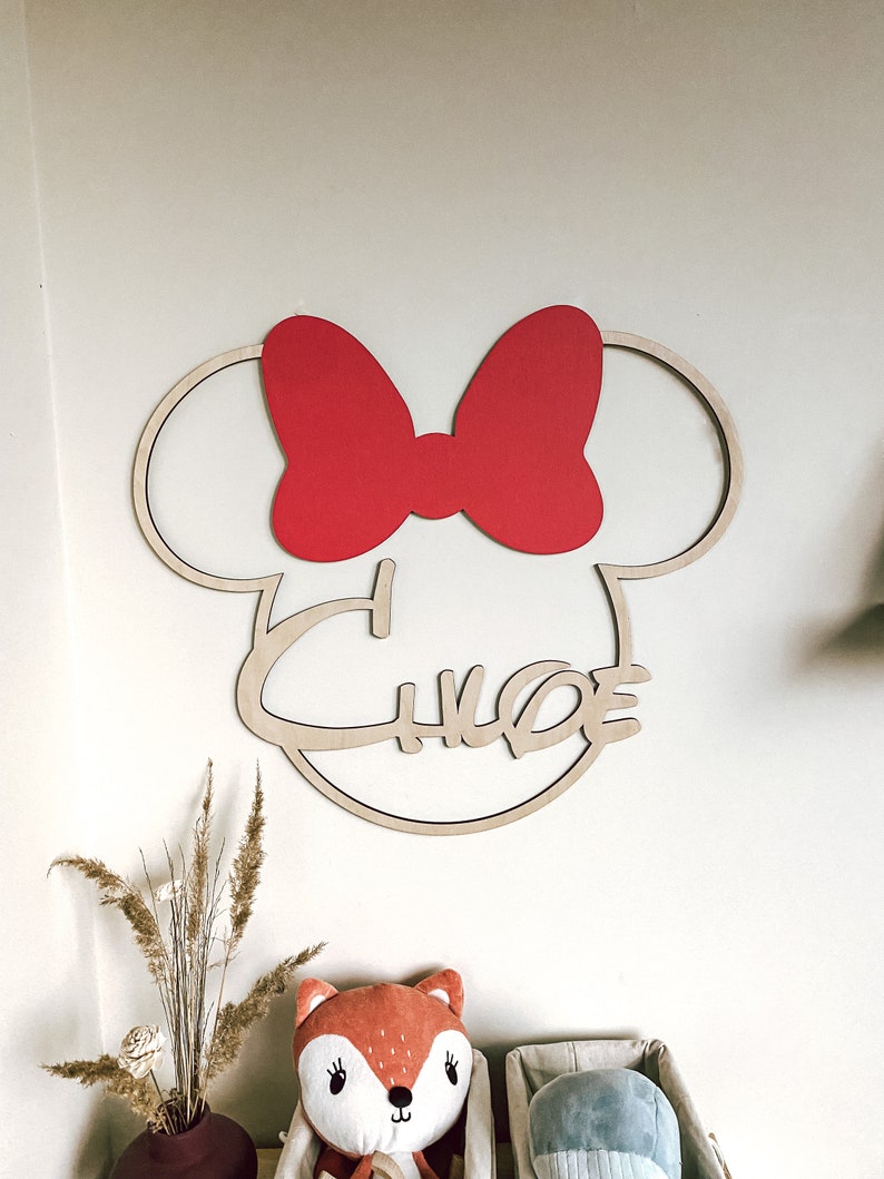 May include: Wooden wall decor featuring a silhouette of Mickey Mouse's head with a red bow and the name "Chloe" written in a cursive font.