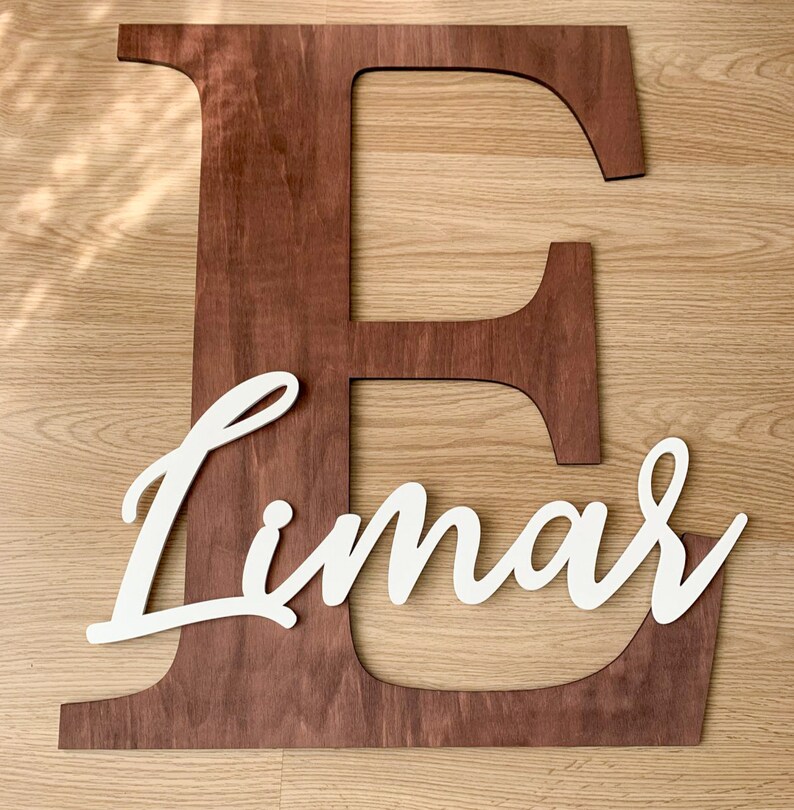 K&ouml;nnte beinhalten: Ein gro&szlig;er Holzbuchstabe E in einer dunkelbraunen Lasur mit dem Namen "Limar" in wei&szlig;er Kursivschrift.
