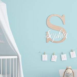 K&ouml;nnte beinhalten: Ein wei&szlig;er Holzbuchstabe S mit dem Namen Sophia in wei&szlig;er Kursivschrift auf der Vorderseite. Der Buchstabe h&auml;ngt an einer hellblauen Wand mit einem wei&szlig;en Kinderbett und einem wei&szlig;en Baldachin im Hintergrund. Unter dem Buchstaben h&auml;ngt eine Schnur mit wei&szlig;en Karten, auf denen das Wort "love" in rosa Kursivschrift steht.