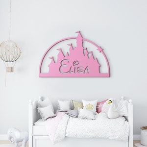 May include: Pink wooden cutout of a castle with the name "ELIZA" in the centre. The castle is in the shape of a half circle and has a star on top.