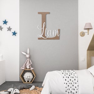 K&ouml;nnte beinhalten: Eine hellgraue Wand mit einem gro&szlig;en Holzbuchstaben L, auf dem der Name Liam in Wei&szlig; geschrieben steht. Die Wand ist mit blauen Sternen verziert. Im Vordergrund steht ein wei&szlig;es Bett mit einer schwarzen und wei&szlig;en Sternen-Bettdecke.
