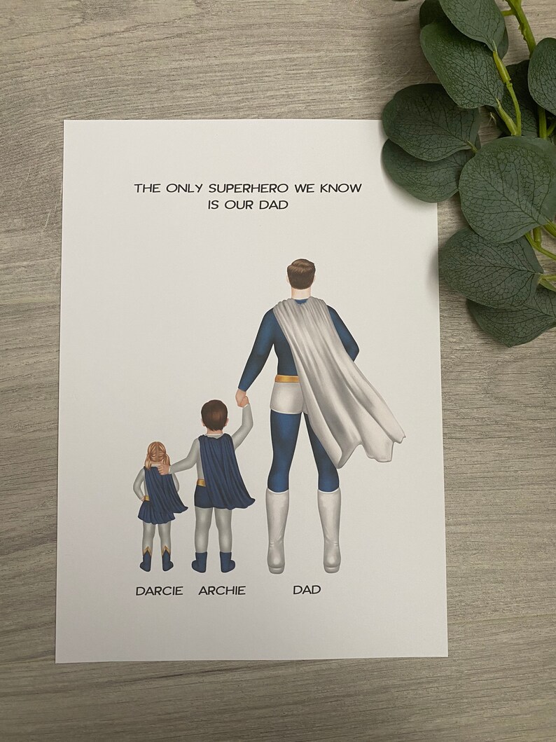 May include: A white card with the text "The only superhero we know is our dad."  A father and two children are illustrated as superheroes, standing back to back. The father is wearing a blue and white superhero costume, the boy is wearing a blue and white superhero costume, and the girl is wearing a blue and yellow superhero costume. The text "Darcie" is below the girl, "Archie" is below the boy, and "Dad" is below the father.