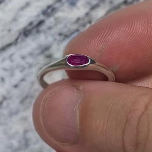 Puede incluir: Un anillo de plata con una pequeña piedra preciosa rosa de forma ovalada engastada en el centro.