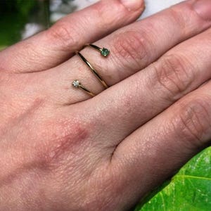 May include: Two gold rings with small gemstones. One ring has a green gemstone and the other has a clear gemstone.