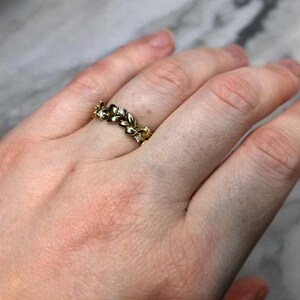 May include: A gold band ring with a delicate leaf design and small clear stones.