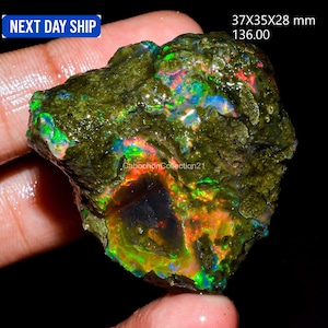 May include: A raw, dark green opal specimen featuring vibrant flashes of red, orange, green, and blue play-of-color across its textured surface. The stone measures 37x35x28 mm and displays a natural, irregular shape with deep, iridescent inclusions.