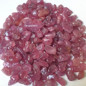 May include: A pile of loose pink ruby gemstones. The rubies are various sizes and shapes, with some having a more pointed shape and others being more rounded.