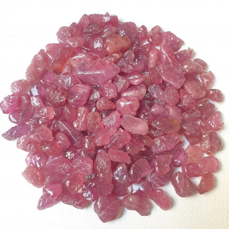 May include: A pile of pink ruby gemstone rough. The rough is in various shapes and sizes. The ruby rough is a natural gemstone.