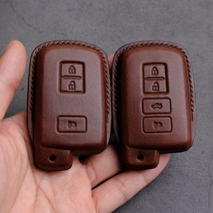 以下が含まれることがあります： ステッチのディテールが施された、茶色の革製のキーカバー2つ。1つのカバーには3つのボタン、もう1つのカバーには4つのボタンがあります。