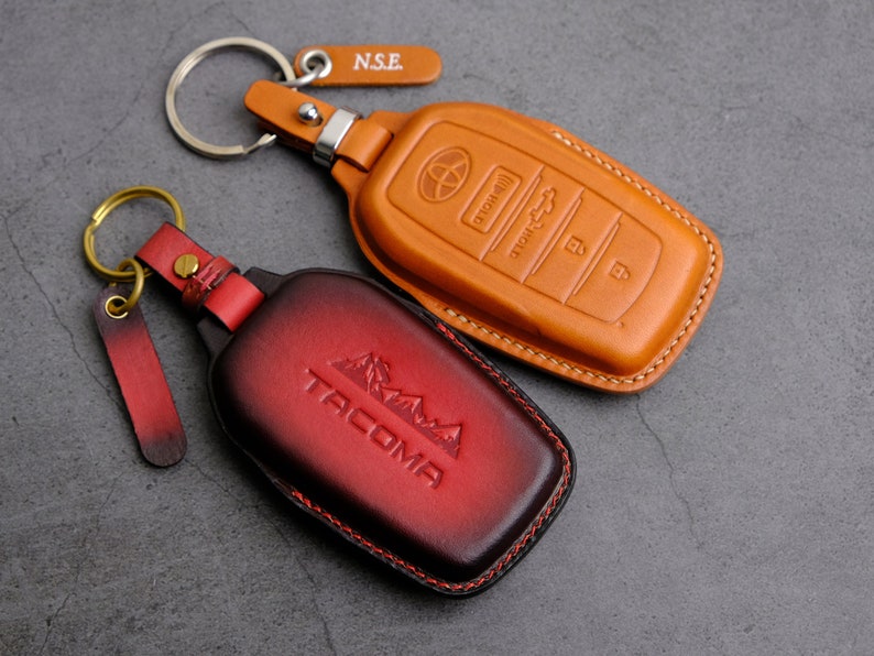 May include: Two leather key fobs with key rings. The fob on the left is red and has the word "TACOMA" embossed on it. The fob on the right is brown and has the words "SMART KEY" embossed on it.