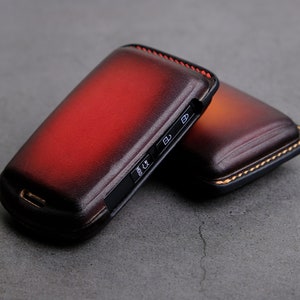 May include: Two leather phone cases with a red and brown ombre design. The cases have a stitched edge and a button on the side.