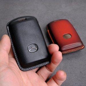 May include: Two leather key fobs, one black and one red, with contrasting stitching. The black key fob has a silver Mazda logo.