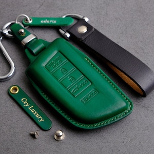 May include: Green leather key fob cover with embossed buttons and the words "ENGINE HOLD" and "EUROLO". Includes a black leather strap, a silver carabiner, and a small green tag with the text "adariz".