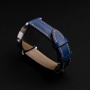 May include: A blue leather watch band with a light brown stitching detail. The band is shown from the side, with the watch face not visible.