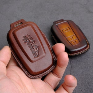 May include: Two brown leather key covers. One cover has the word "4RUNNER" embossed on it. The other cover has three buttons.